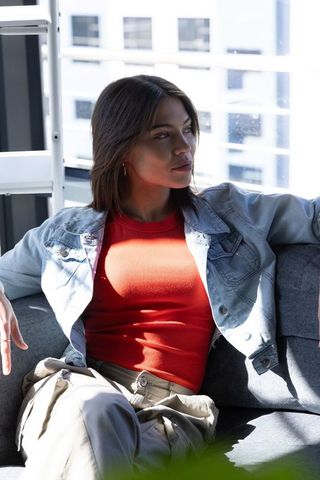 Young woman lounging on couch in sunlit modern apartment wearing denim jacket and red top