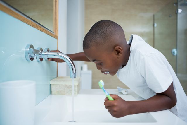 Young boy brushing teeth in modern bathroom. Ideal for topics on children's hygiene, dental care, morning routines, and healthy habits. Suitable for educational materials, parenting blogs, and health-related content.