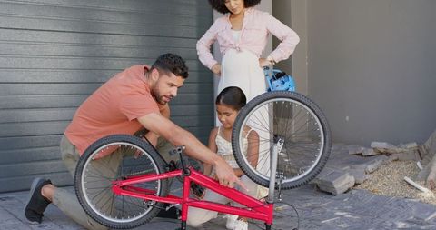 Father Repairing Bicycle with Daughters' Help Outdoors