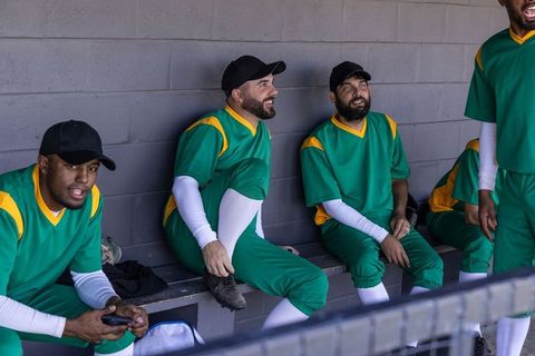 Baseball team relaxing in dugout chatting and tying cleats between innings