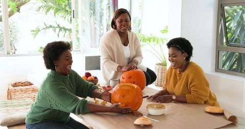 Women Joyfully Carving Pumpkins in Sunlit Craft Room