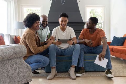 Multiracial friends laughing, watching tablet and sharing ideas in cozy living room