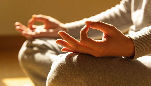Practicing gyan mudra meditation cross-legged in sunlit room in grey loungewear focus