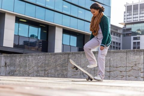 Young woman practicing skateboard trick on urban plaza with modern glass buildings