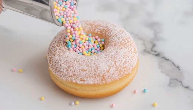 Pouring pastel nonpareils into powdered sugar donut close-up on marble countertop