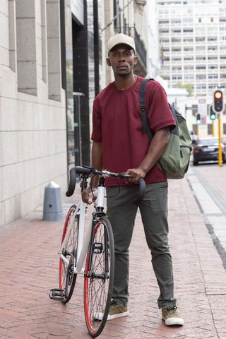 African american man standing with road bicycle on urban sidewalk, maroon shirt and cap