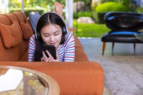 Young Woman Relaxing with Smartphone and Headphones on Bright Orange Sofa