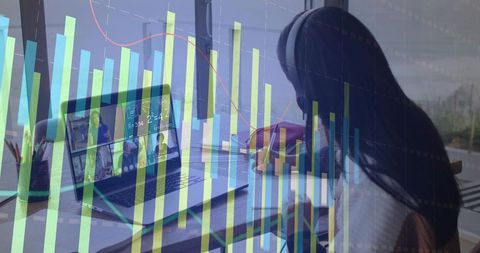 Woman writing with headphones at laptop and notebook, analytics chart overlay, remote work focus