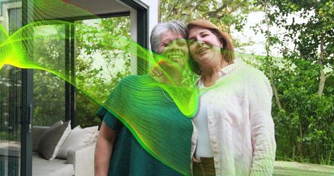 Senior women embracing on patio with green ribbon overlay, outdoor family wellness