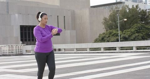 Woman checking smartwatch while walking on urban plaza in purple top