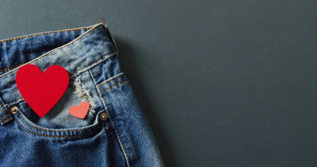 Close up of jeans with red hearts on grey background with copy space. Denim day, material, style and design concept.