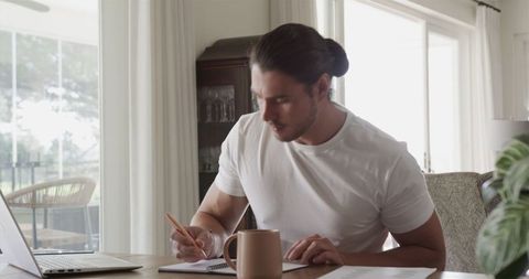 Focused Young Man Working on Laptop with Notepad and Coffee