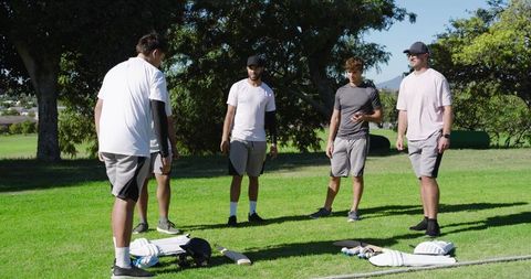 Diverse cricket teammates standing on grass discussing strategy and preparing gear