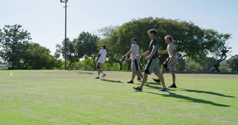 Male teammates walking across grassy field practicing ultimate frisbee on sunny day
