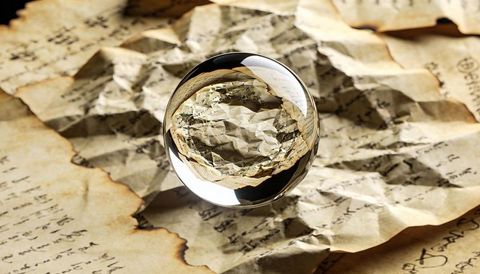 Glass orb magnifying crumpled antique manuscript with singed edges and warm sepia light