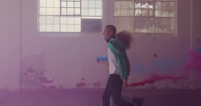 This scene captures a dynamic moment where a young man and woman run energetically through an empty warehouse with colored smoke bombs. The vibrant atmosphere embodies creativity, freedom, and youthful spirit. Ideal for use in campaigns or advertisements highlighting bold expression, multiculturalism, or urban settings.