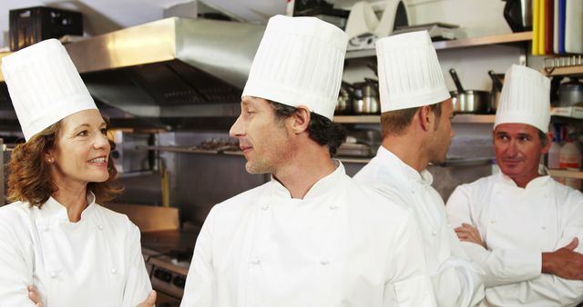 Professional chefs in white uniforms and hats are seen discussing in a busy commercial kitchen. The image showcases teamwork, communication, and collaboration in a bustling restaurant setting. Ideal for articles or posts related to culinary arts, professional cooking, and restaurant management, or marketing materials for culinary schools and kitchen equipment suppliers.