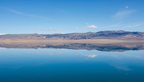Glassy high-plain lake reflecting rolling hills and clear blue sky in minimalist panorama
