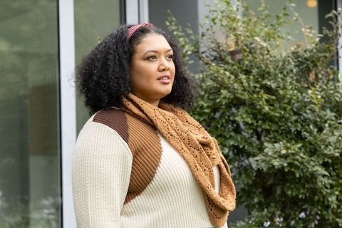 Thoughtful asian woman standing outdoors wearing cozy sweater and knitted scarf near glass window