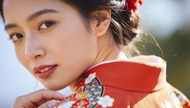 Turning woman wearing red floral kimono touching collar and showing kanzashi
