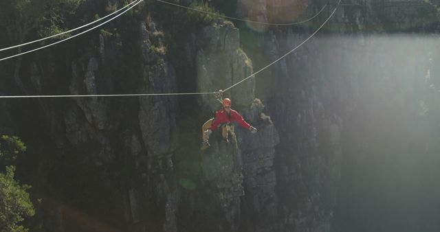 Man ziplining over a deep canyon, showcasing adventure and thrill of extreme sports. Safety gear adds element of security. Suitable for promoting outdoor activities, adventure tourism, and recreational sports ads.