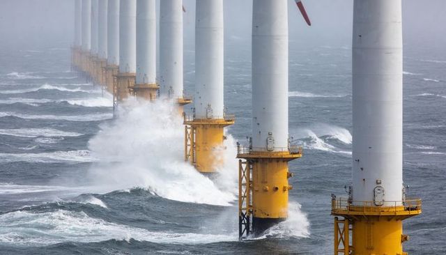 Offshore wind turbines standing in rough sea with yellow monopile platforms