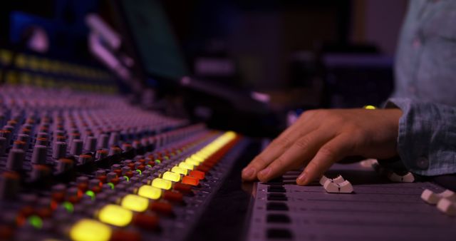 Close-up view of an audio engineer's hand adjusting controls on a soundboard in a recording studio. Ideal for use in projects related to music production, professional audio engineering, and studio recording environments.