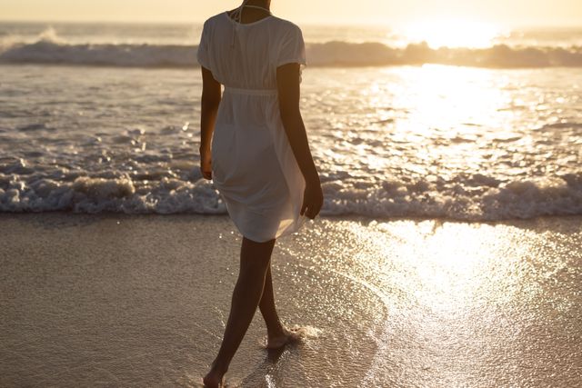 This image captures a woman walking towards the sea during sunset, creating a serene and peaceful atmosphere. Ideal for use in travel blogs, vacation advertisements, wellness and relaxation content, and nature-themed projects.