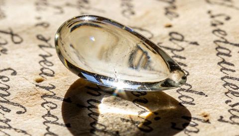 Clear oval glass cabochon magnifying cursive handwriting on aged parchment casting sparkle