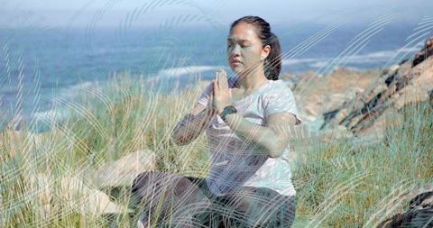 Woman meditating outdoors on coastal slope with fitness tracker