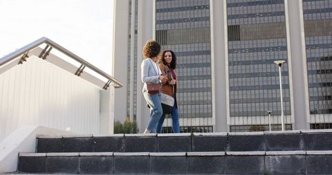 Two African American Women Walking and Talking on Urban Plaza Steps with Crossbody Bags