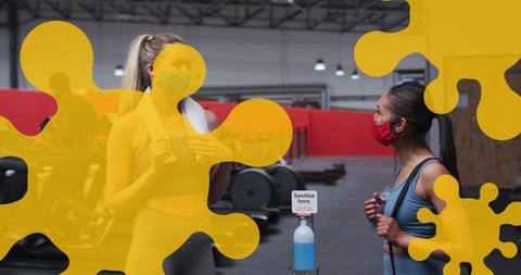 Two women wearing masks talking at gym sanitizer station during workout session