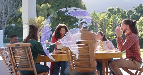 Friends sharing outdoor dinner on sunny patio with holographic globe overlay for connection