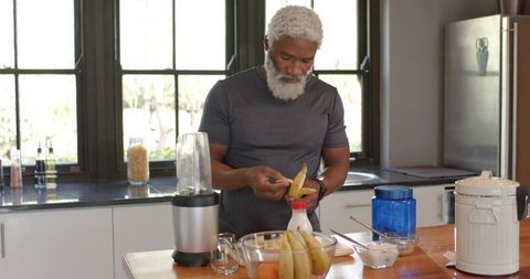 Senior Man Prepares Smoothie in Modern Kitchen with Fresh Ingredients