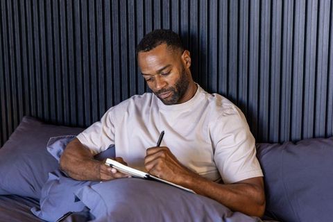 Man writing journal in bed during morning routine for mindful reflection