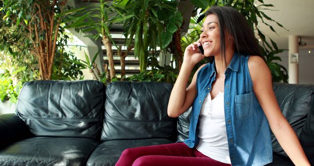 Smiling woman talking on phone while sitting on sofa in bright living room - Download Free Stock Images Pikwizard.com