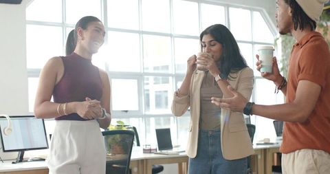 Multicultural coworkers chatting and sipping coffee in modern bright open-plan office