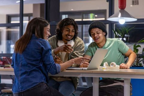 Multicultural college students collaborating on laptop in modern study lounge