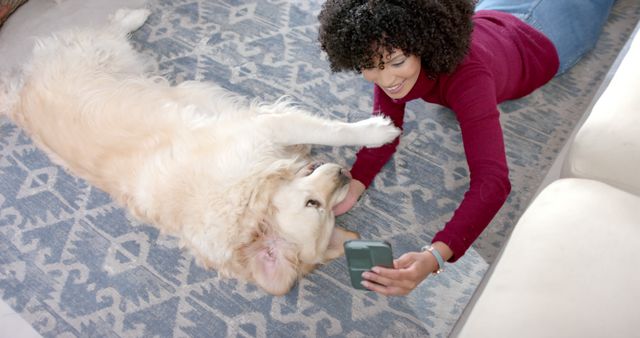 This image depicts a woman laying on a cozy rug taking a selfie with her happy golden retriever. Both appear relaxed and are enjoying their time together. This visual can be used for promotions related to pet care, lifestyle, social bonding, and mobile phone products.
