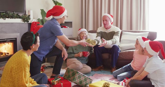 A family gathers in a cozy living room to open Christmas presents. Adults and children are wearing Santa hats, sitting around a coffee table next to a decorated fireplace. This vibrant and warm atmosphere is perfect for holiday greeting cards, festive advertisements, or articles about family traditions during Christmas.