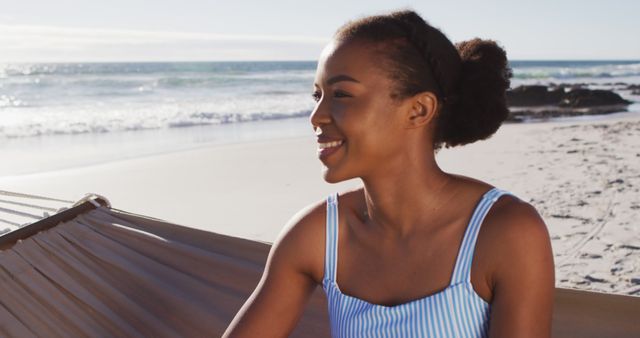 Close up of african american woman smiling while sitting on a hammock at the beach. travel vacation lifestyle concept