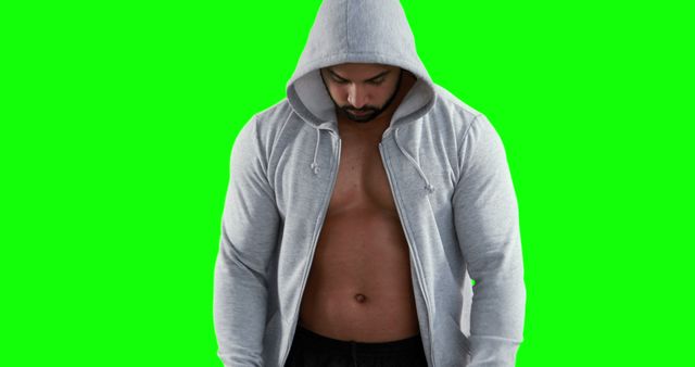 Fit man wearing gray hoodie looking down, chest and abs visible, standing against green screen background. Useful for fitness, workout, advertisements, and health-related content.
