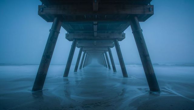 Under-pier symmetry revealing foggy blue seascape with reflecting wet sand and pylons