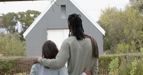 Back view diverse couple embracing in garden before small gray shed