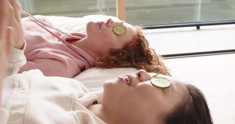 Diverse friends relaxing with cucumber eye slices on low bed near sunlit window