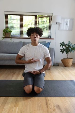 Meditating Hispanic Man Kneeling on Yoga Mat in Calm Living Room Setting