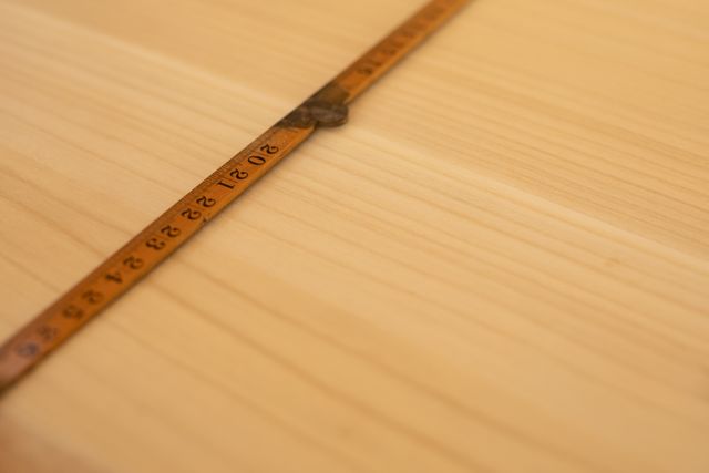 The measuring tape of a surfboard maker lying on the smooth wooden surface of a surboard being made on a workbench in a workshop, after smoothing with a sander.