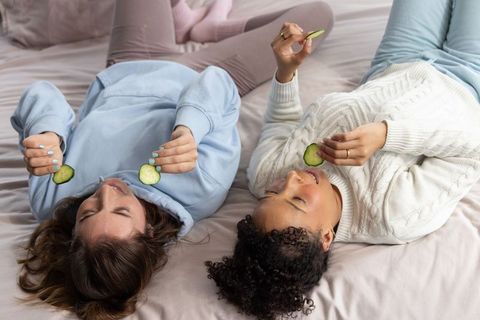 Reclining friends enjoying cozy at-home spa night with cucumber slices and loungewear