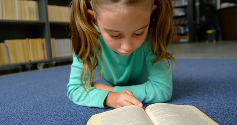 Young schoolgirl reading book on library floor for learning and education