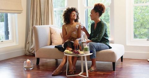 Two friends toasting on beige chaise lounge in bright modern living room
